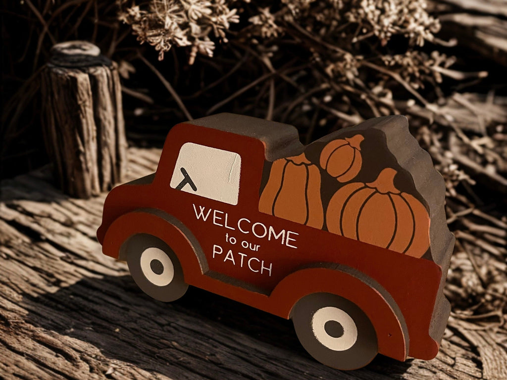 Welcome to Our Patch red truck sitter on weathered wood with dried botanicals in moody fall light