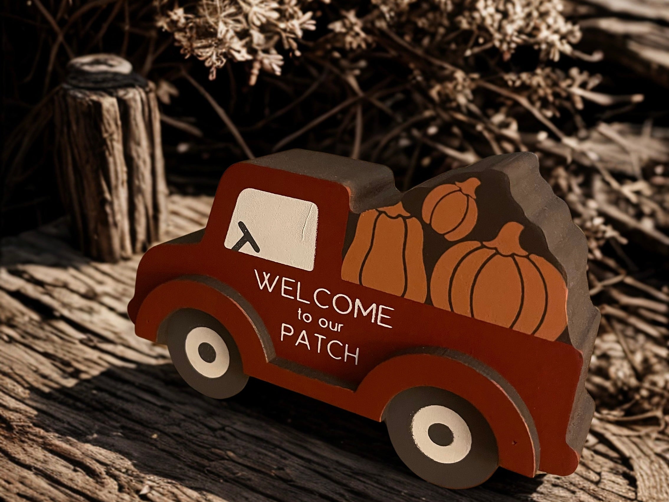 Welcome to Our Patch red truck sitter on weathered wood with dried botanicals in moody fall light