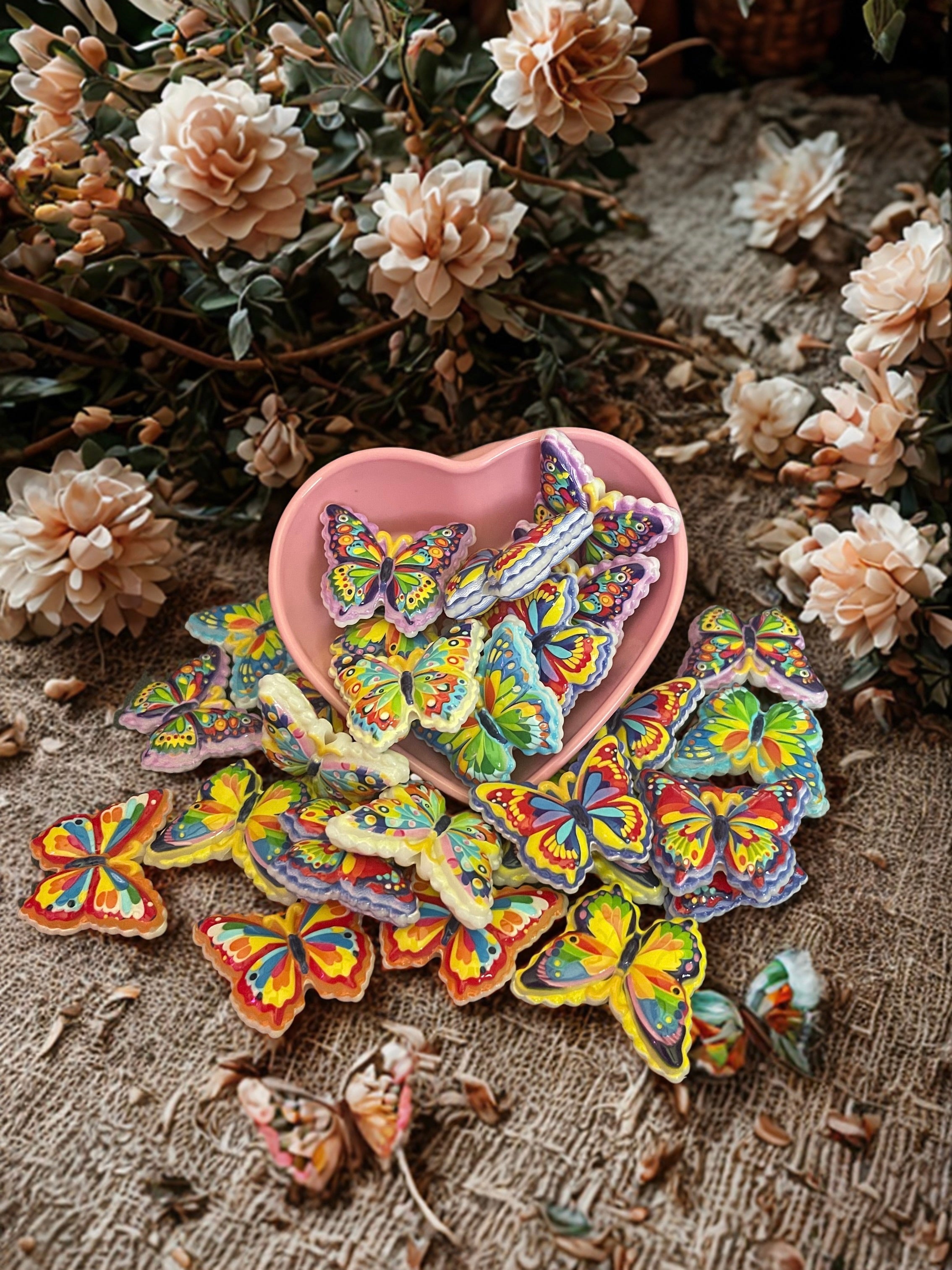 Rainbow butterfly beads in a pink heart bowl surrounded by dried flowers