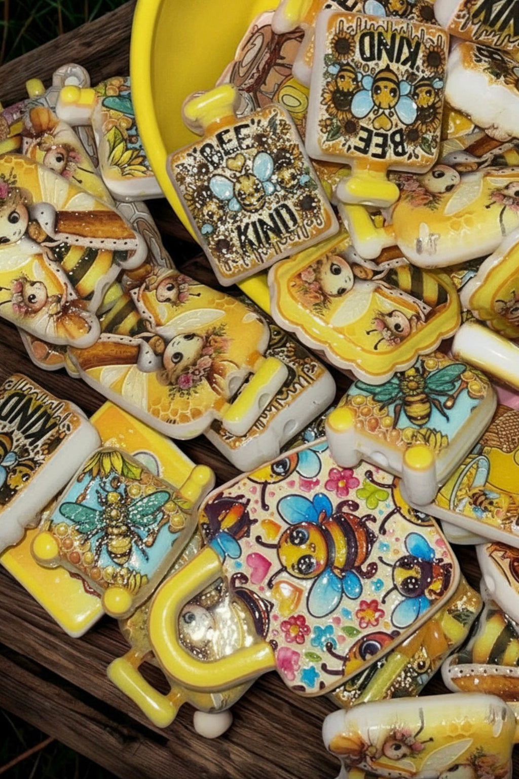 Honey bee bead charms spilling from yellow bowl on wood surface