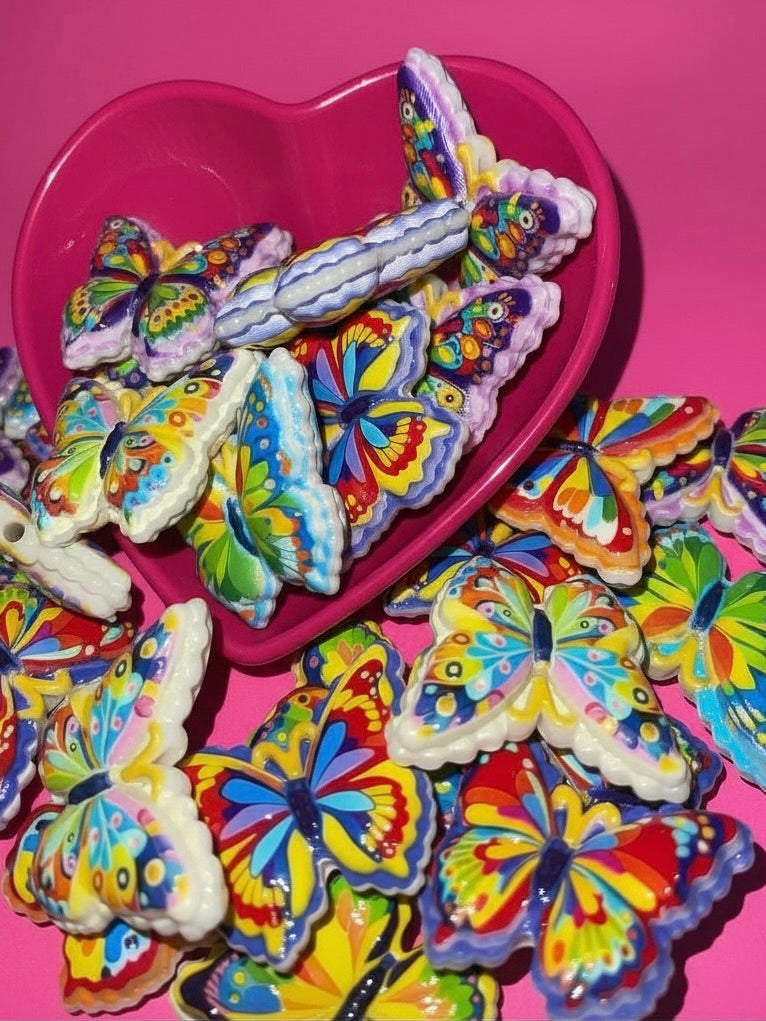 Colorful rainbow butterfly beads spilling from a pink heart bowl on hot pink background