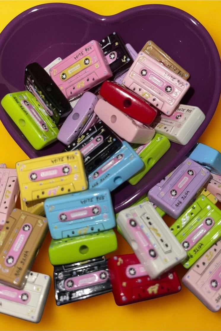 Mixed color cassette tape beads in a purple heart bowl on yellow background