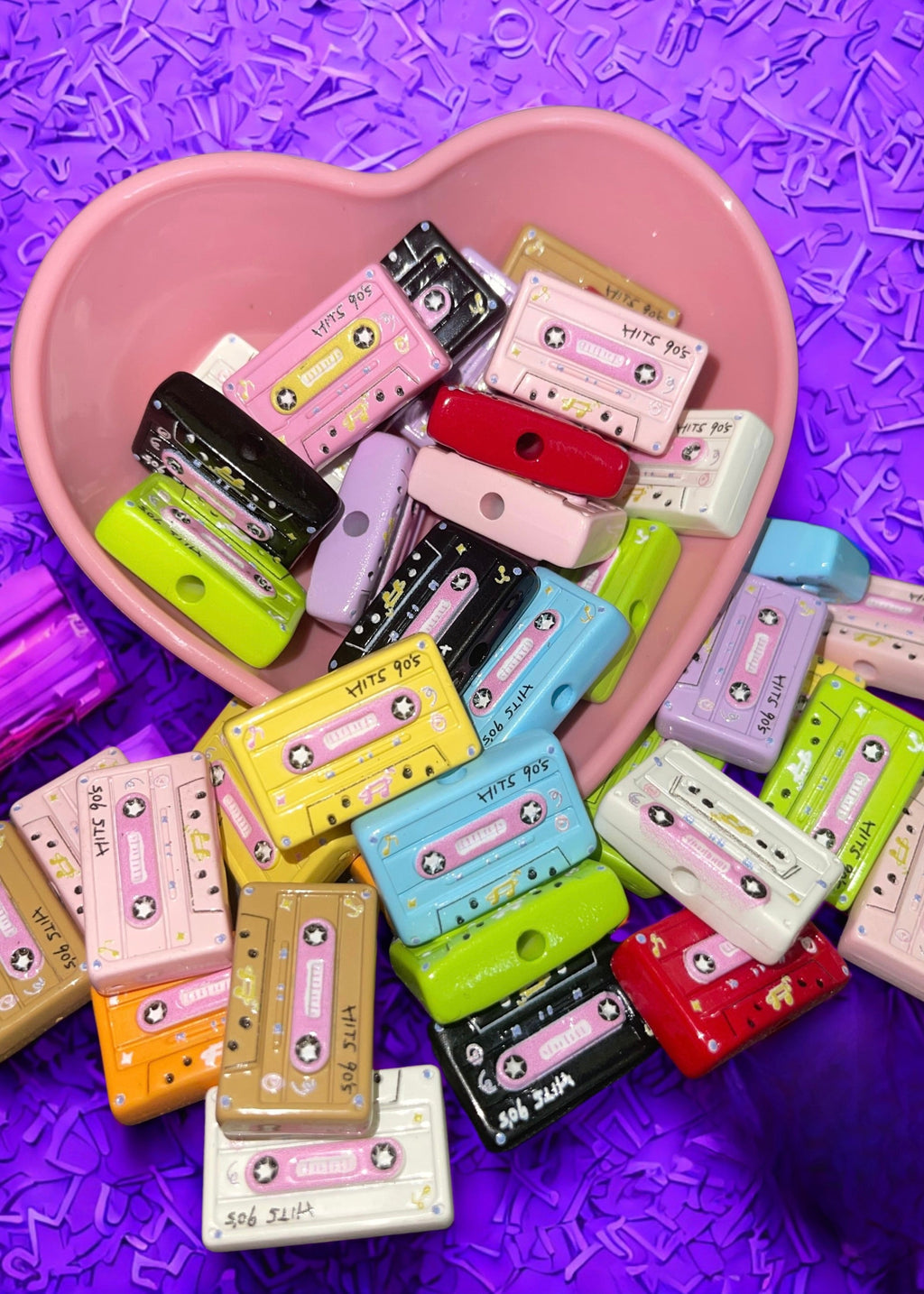 Retro cassette tape beads in assorted colors in a pink heart bowl on purple background