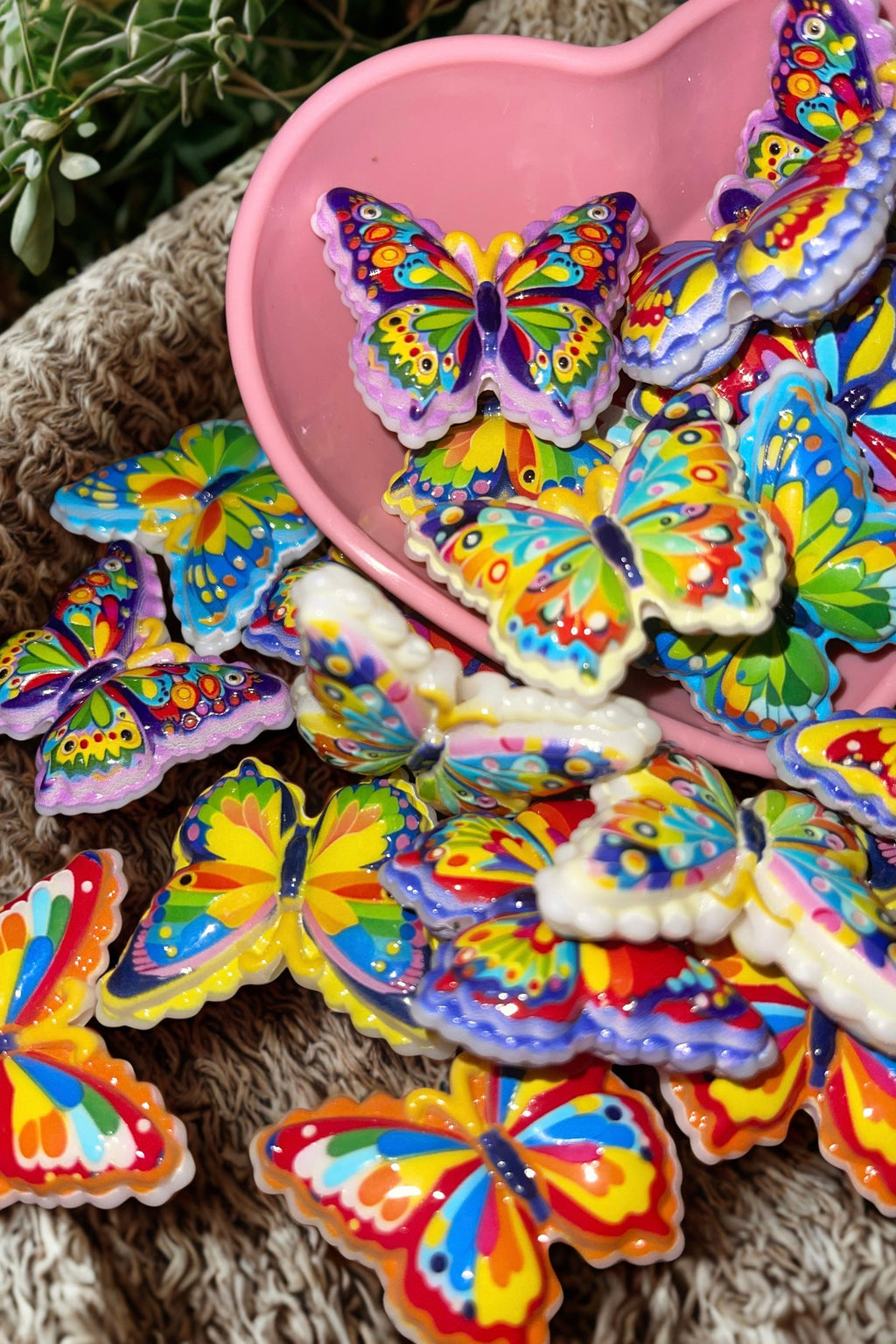 Vibrant butterfly beads in a pink heart bowl on rustic burlap with flowers