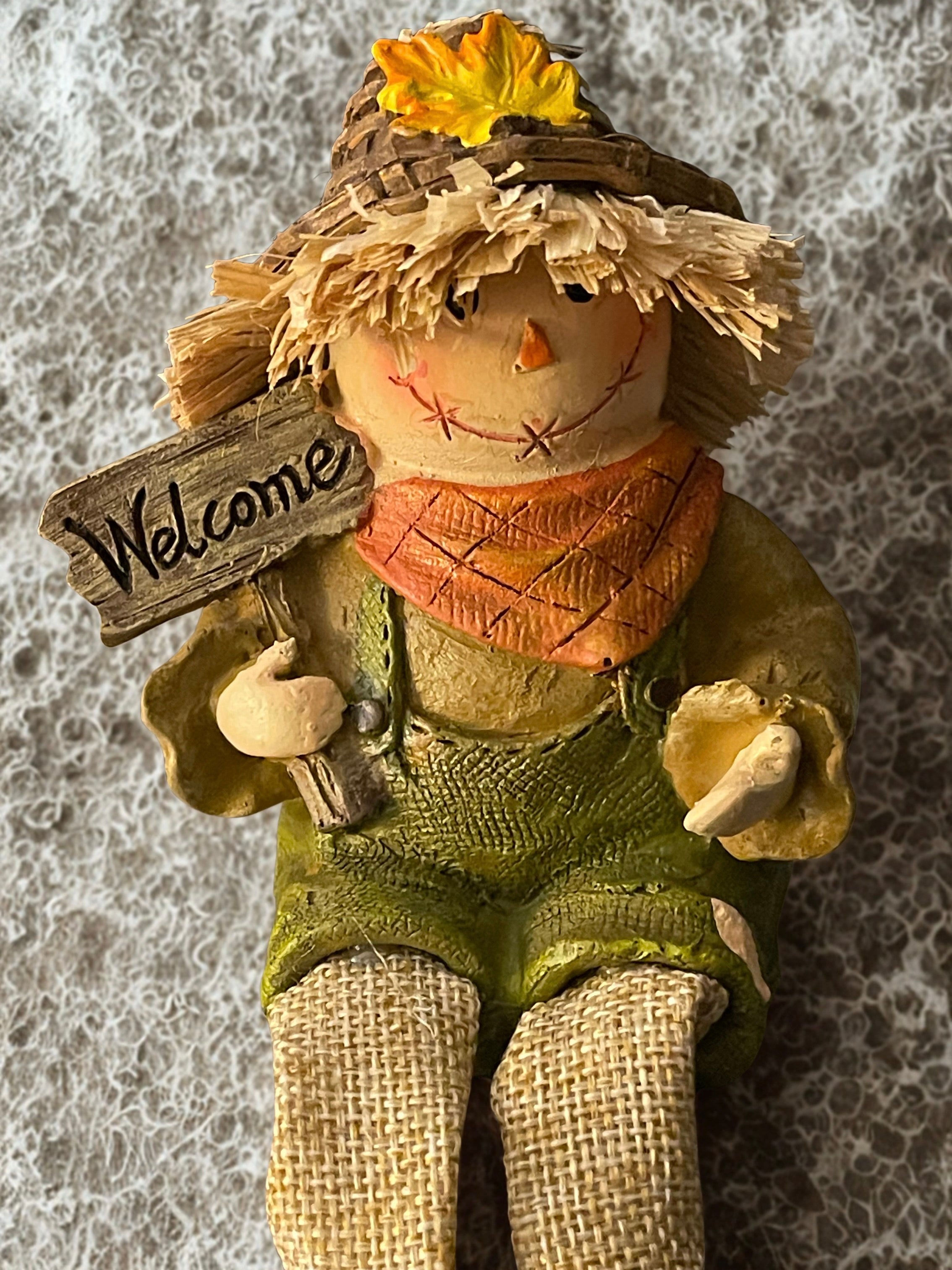 Corn scarecrow dangle leg shelf sitter seated on white pedestal with grey background