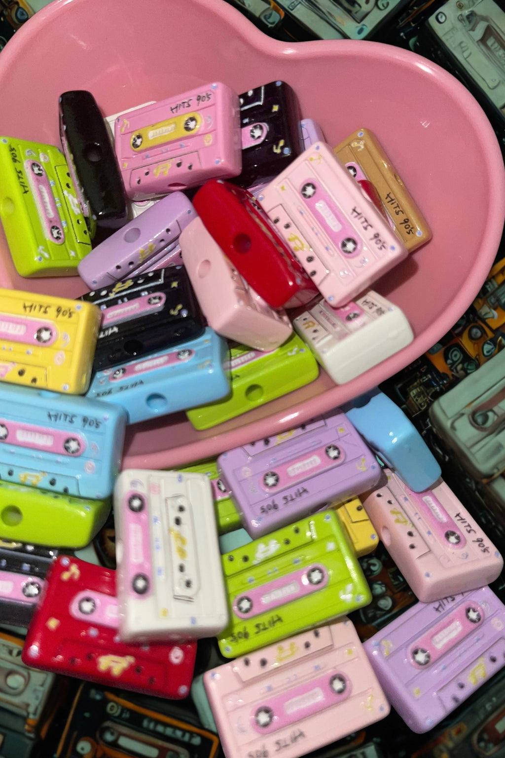 Colorful cassette tape beads spilling from a pink heart bowl on teal cassette backdrop