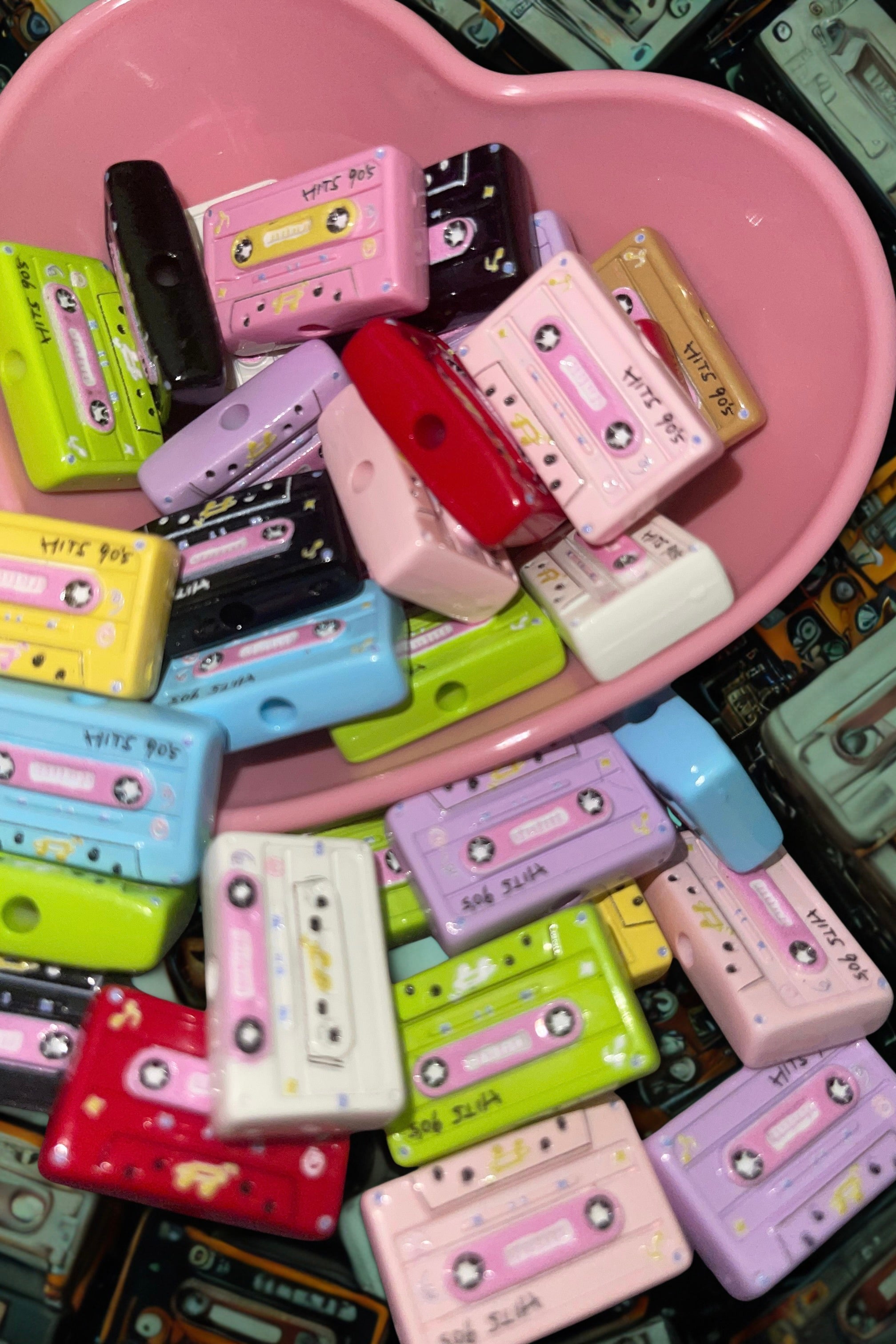 Colorful cassette tape beads spilling from a pink heart bowl on teal cassette backdrop