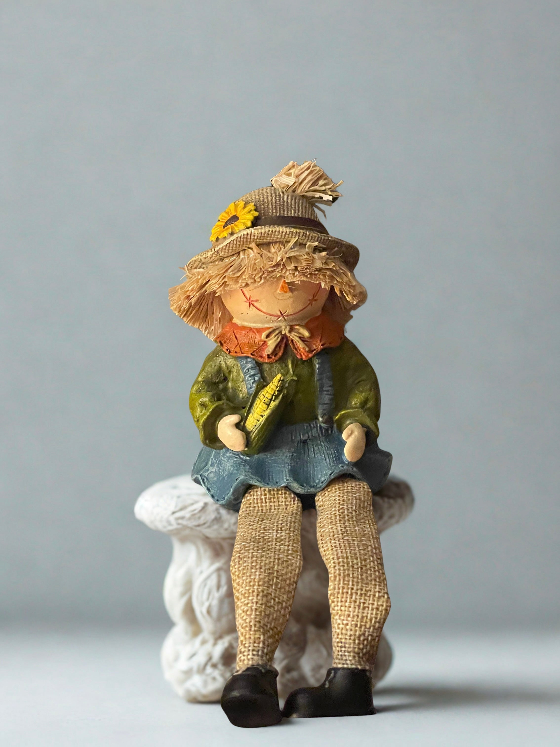 Pumpkin scarecrow dangle leg shelf sitter seated on white pedestal with blue-grey background